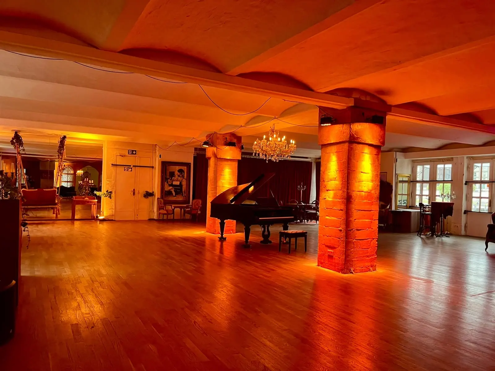 Der Saal des Tangoloft in orangem Licht, mit Flügel, Kronleuchter und Säulen